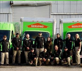 Smiling Production staff in SERVPRO uniforms, in front of company trucks