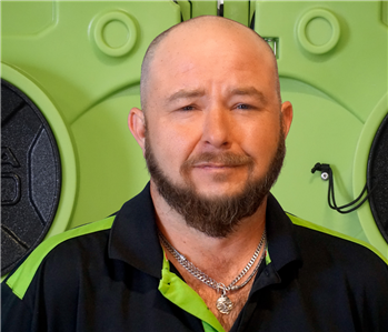 Bald man with beard waering a SERVPRO shirt standing in front of drying equipment