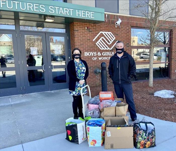 Man and woman outside of Boys Club front doors with boxes and bags of food for donation